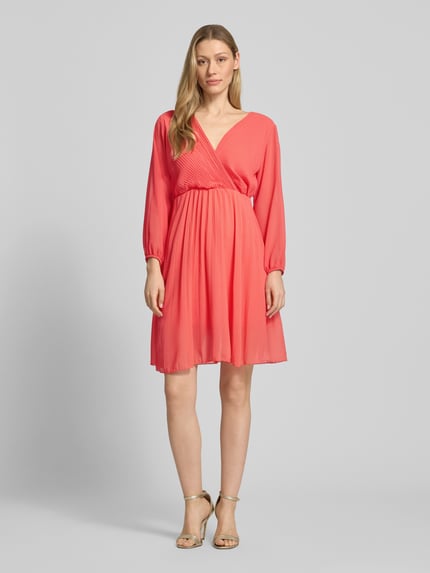 Frauenmodel trägt Kleid aus Viskose-Mix mit V-Ausschnitt von ZABAIONE in koralle, Tailliert, langärmelig, Semitransparent, blickdichter Unterrock, Ganzkörperansicht von vorne. Rückenlänge 94 cm, Brustweite 45 cm, Ärmellänge 56 cm, Größe S.
