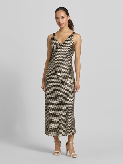 Frauenmodel trägt Midikleid mit V-Ausschnitt Modell 'Qova wave' von Someday, Satin, Straight Fit, schwarz-gold gemustert, Ganzkörperansicht von vorne.