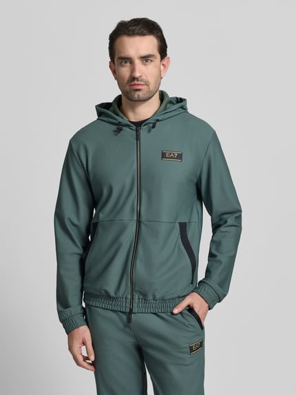 Mężczyzna nosi Regular Fit Sweatjacke mit Logo-Patch od EA7 Emporio Armani, elastyczna mieszanka materiałów, fakturowany wzór, naszywka z logo, kaptur z tunelem, wpuszczane kieszenie, zamek błyskawiczny dwustronny, elastyczne wykończenia, długość tyłu w rozmiarze M: 68 cm, długość rękawów w rozmiarze M: 67 cm, widok całej sylwetki z przodu.