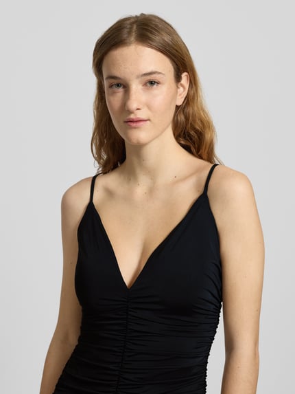 Vrouwenmodel draagt Slim Fit avondjurk met plooien model 'Lavanda' van Bardot in zwart, V-hals, spaghetti bandjes, close-up bovenlichaam.