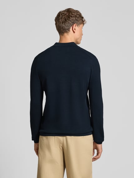 Männermodel trägt Poloshirt mit Logo-Stitching von MARC O'POLO in Dunkelblau, Strickoptik, langarm, Ganzkörperansicht Rückansicht.