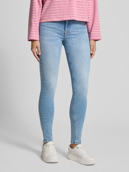 Kobieta nosi Skinny Fit Jeans aus Baumwoll-Mix Modell 'NORA' von Tommy Jeans w jasnoniebieskim kolorze, gładka faktura materiału, widok całej sylwetki z przodu, damskie Skinny Fit Jeans od Tommy Jeans.