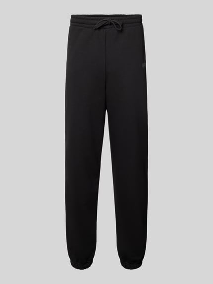 Produktfoto, spodnie dresowe Sweatpants mit Label-Print von Alpha Industries, czarny kolor, elastyczny pas z tunelem, mieszanka bawełny, luźny krój, wpuszczane kieszenie, nadruk z logo, długość wewnętrzna nogawki w rozmiarze M: 44 cm