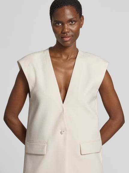 Frauenmodel trägt Weste mit V-Ausschnitt und Pattentaschen von Copenhagen Muse in Creme, Material-Mix mit Viskose-Anteil, Regular-Fit, Nahaufnahme Oberkörper. Rückenlänge 78 cm, Schulterbreite 46 cm, Brustweite 51 cm bei Größe S.