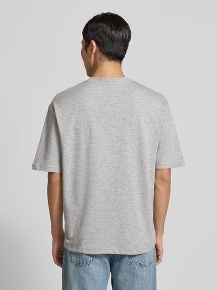 Męski model nosi Oversized Shirt aus Baumwoll-Mix Modell 'LOOSEOSCAR' od SELECTED HOMME, jednokolorowy melanż, krój oversized, wyhaftowane logo, okrągły dekolt, krótki rękaw, drobne prążkowanie, mieszanka bawełny; widok całej sylwetki od tyłu.