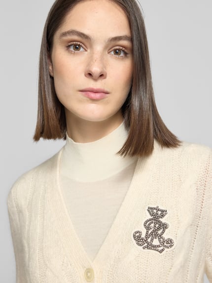 Frauenmodel trägt Cardigan aus Mohair mit Logo-Applikation von LAUREN RALPH LAUREN, cremefarbener Zopfmusterstrick, Knöpfe, Strass, Nahaufnahme Oberkörper.