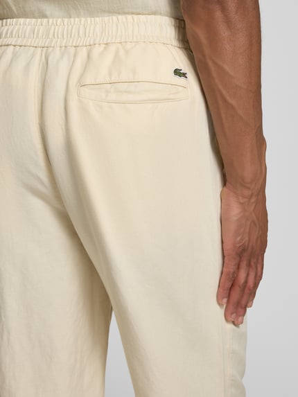 Mężczyzna nosi Straight Leg Stoffhose aus Leinen-Mix von Lacoste, beżowy kolor, flammgarn, z gumką w pasie, detal tyłu, detalaufnahme.