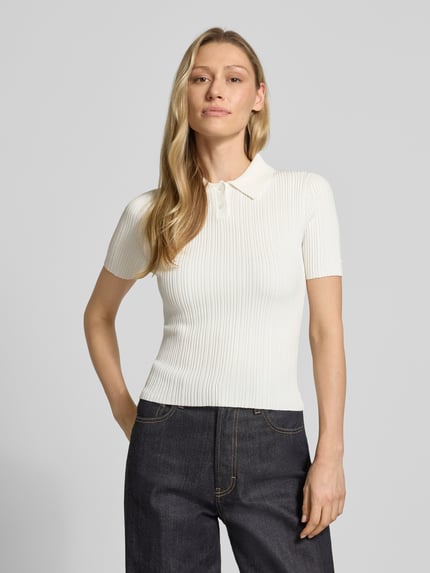 Frauenmodel trägt Slim Fit Strickpullover aus Viskose-Mix Modell 'Sareplette' von HUGO, Strickoptik, Streifen-Struktur, Polokragen, V-Ausschnitt, Kurzarm, Materialverarbeitung: Strick, Farbe creme, Ganzkörperansicht von vorne.