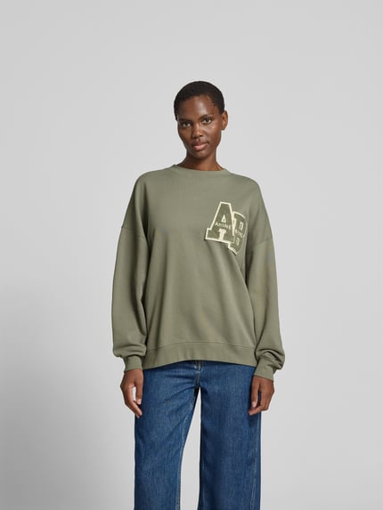 Frauenmodel trägt Relaxed Fit T-Shirt mit Logo-Print von Anine Bing aus reiner Baumwolle in Olivgrün, Rundhalsausschnitt, eingefasste Ärmelabschlüsse, Rückenlänge 60 cm, Ganzkörperansicht von vorne.
