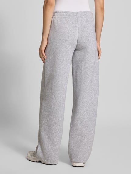 Frauenmodel trägt Sweathose in grau melange mit geradem Bein von REVIEW, Baumwoll-Mix, elastischer Bund, Logo-Print, Ganzkörperansicht Rückansicht.
