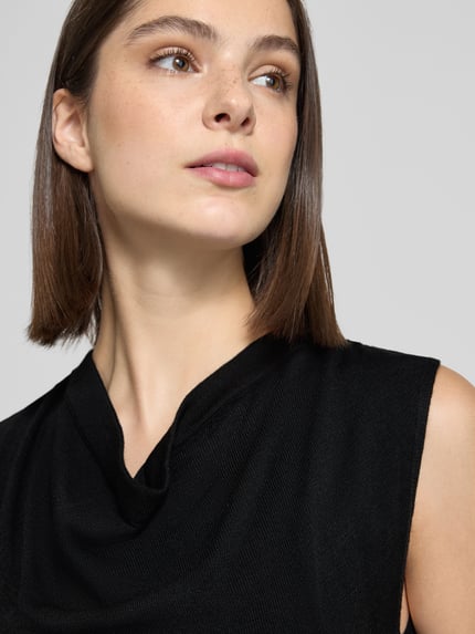 Frauenmodel trägt Strickkleid mit Wasserfall-Ausschnitt Modell 'SANTA' von MANGO in Schwarz, feine Textur, Nahaufnahme Oberkörper. Gerader Schnitt, Midikleid, Rückenlänge bei Größe S 113 cm, Brustweite 37 cm.