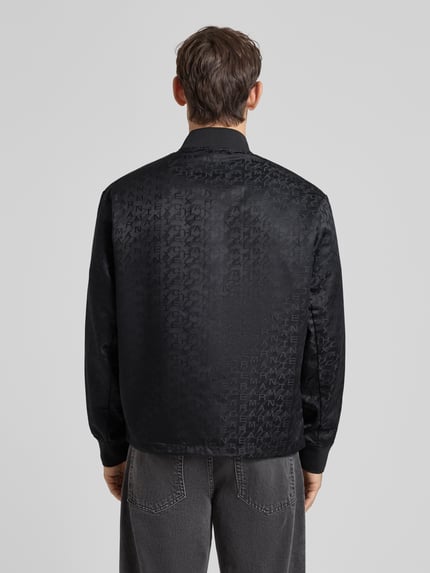 Männermodel trägt schwarzen Blouson mit Zweiwege-Reißverschluss von ARMANI EXCHANGE, Gerader-Schnitt, Stehkragen, Ganzkörperansicht Rückansicht. Rückenlänge 67 cm, Schulterbreite 51 cm, Brustweite 61 cm, Ärmellänge 66 cm, gerippte Ärmelabschlüsse.