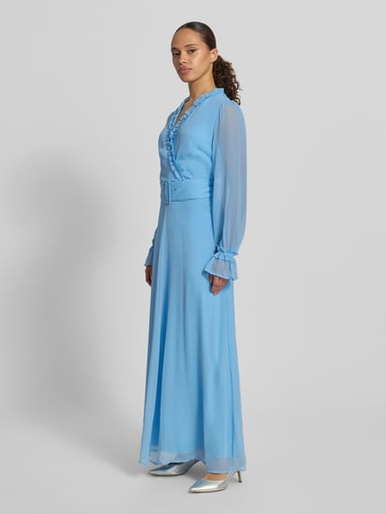 Frauenmodel trägt Maxikleid mit Gürtel und Rüschen Modell 'EMMA' von Vila in Hellblau aus Chiffon, A-Linie, Ganzkörperansicht von vorne.