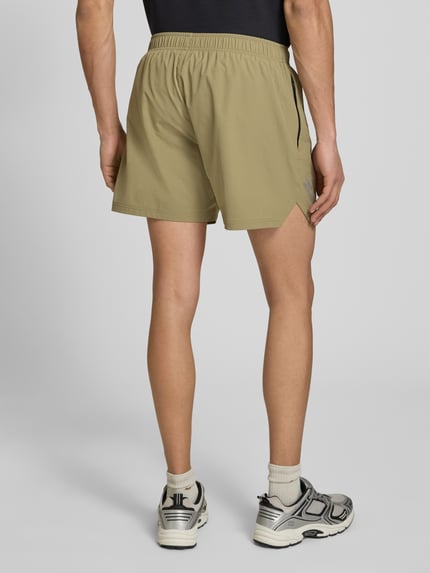 Mężczyzna nosi Shorts mit elastischem Bund und Label-Print od HALO w kolorze beżowym, krój regular fit, materiał stretch, szerokość w rozmiarze M 39 cm, długość wewnętrzna nogawki 13 cm, nadruk z logo, widok całej sylwetki z tyłu.