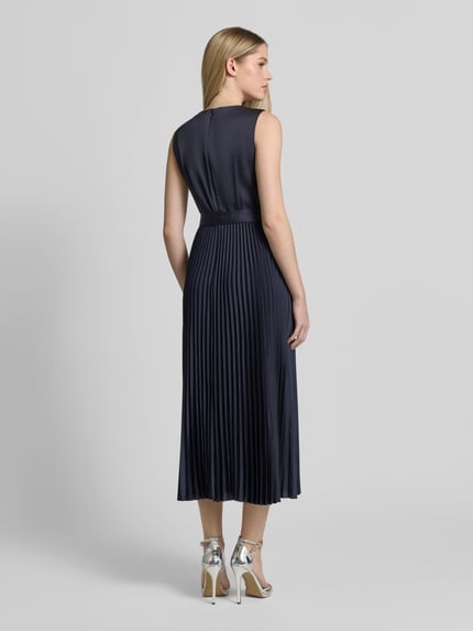Frauenmodel trägt Cocktailkleid mit Plisseefalten von Vera Mont in Dunkelblau mit Taillenband, Midilänge, Ganzkörperansicht Rückansicht.