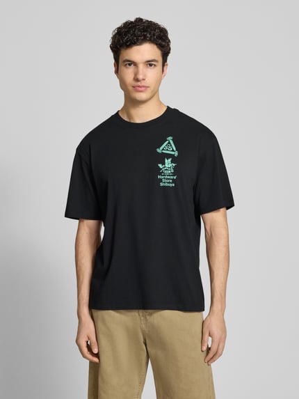 Männermodel trägt T-shirt met print en ronde hals van Edwin in zwart van puur katoen, relaxed fit, ruglengte maat M 72 cm, Ganzkörperansicht van voren