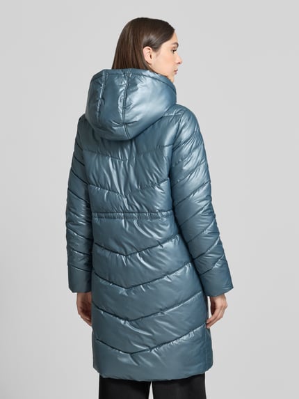 Frauenmodel trägt Steppmantel mit Kapuze Modell 'Jacket-Fa44ncy' von ZABAIONE in glänzendem Metalic-Blau mit Teilungsnähten, Ganzkörperansicht Rückansicht.