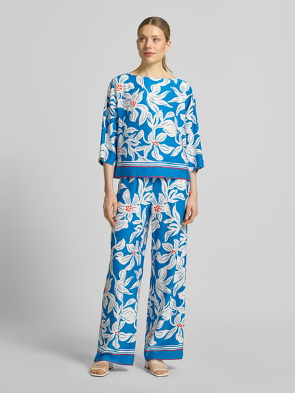Vrouwenmodel draagt stoffen broek van viscose model 'Rylie' van GUIDO MARIA KRETSCHMER WOMAN, relaxed fit, all-over look, elastische band, bandwijdte maat 36: 36 cm, binnenbeenlengte maat 36: 77 cm, blauw met groot wit bloemmotief, gladde textuur. Volledig vooraanzicht.