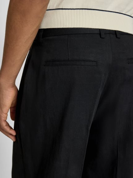 Männermodel trägt Hose mit Bügelfalten Modell 'Reece' von Les Deux, Lyocell-Baumwoll-Mix, schwarze Farbe, Nahaufnahme Rückansicht.