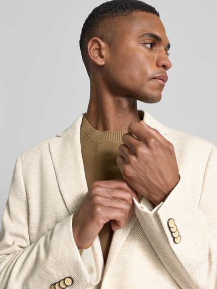 Männermodel trägt Slim Fit 2-Knopf-Sakko mit Pattentaschen von MCNEAL im Strukturmuster und Reverskragen, Nahaufnahme Oberkörper.