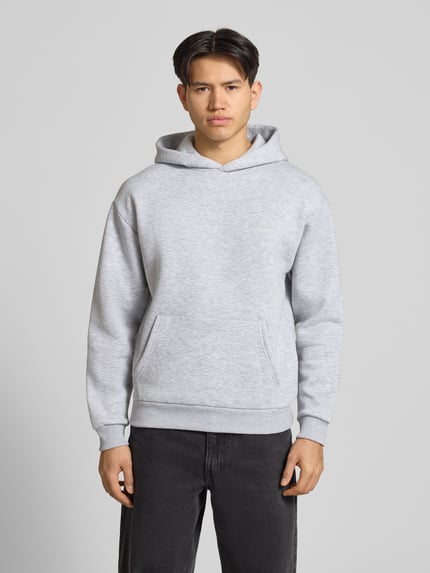 Männermodel trägt Hoodie mit Känguru-Tasche van REVIEW in lichtgrijs, katoenmix, los model, capuchon, labeldetail, elastische boordjes, ganzkörperansicht von vorne.