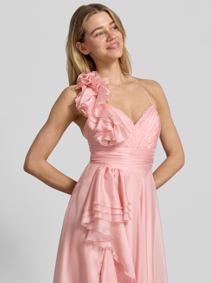 Kobiece modelka nosi 'Abendkleid mit Volants und Herz-Ausschnitt' od V.M., satyna, kolor jasnoróżowy, linia A, maksisuknia, sercowy dekolt, tylne skrzyżowane cienkie ramiączka, falbany, zapięcie na zamek i haftkę z tyłu, długość tyłu w rozmiarze 36: 122 cm, szerokość w rozmiarze 36: 32 cm, widok na górną część ciała z przodu.