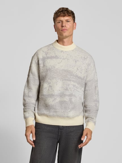 Männermodel trägt Pullover mit geripptem Rundhals Modell 'Kastet' von BOSS Orange, abstraktes Allover-Muster, Strickoptik, Ganzkörperansicht von vorne.