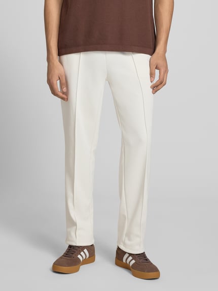 Mannenmodel draagt trainingsbroek met Längsnähten model 'Motus' van Pegador in katoenmix, relaxed fit, elastische band, binnenbeenlengte maat M 75 cm, recht model, witte kleur, detailopname voorkant.