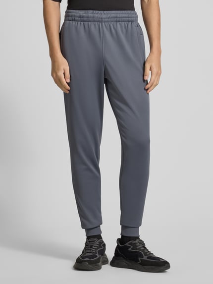 Männermodel trägt Sweatpants mit elastischem Bund von Under Armour in Grau, lockerer Schnitt, Eingrifftaschen, Ganzkörperansicht von vorne.