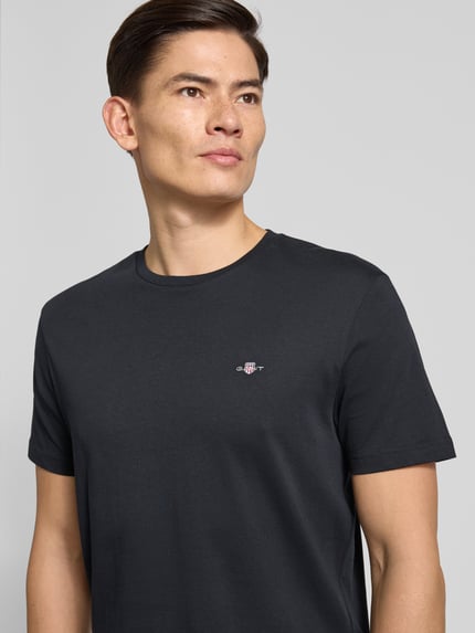 Männermodel trägt Regular Fit T-Shirt mit Label-Stitching Modell 'SHIELD' von GANT in Unifarben-Design aus reiner Baumwolle, Nahaufnahme Oberkörper.