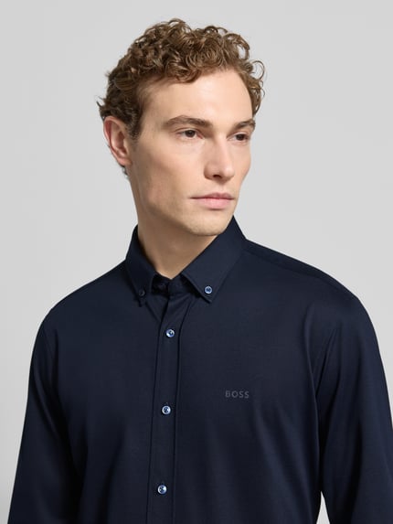 Männermodel draagt Regular Fit Businesshemd uit Pinpoint met stretch van BOSS, donkerblauw katoenmix, logo-opschrift, knoopsluiting, ademend, onderhoudsarm, sneldrogend, nahaufnahme bovenlichaam.