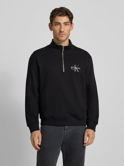 Männermodel trägt Regular Fit Sweatshirt mit Logo-Stitching Modell 'Terry' von Calvin Klein Jeans, Schwarz, Troyer-Kragen, Ganzkörperansicht von vorne.