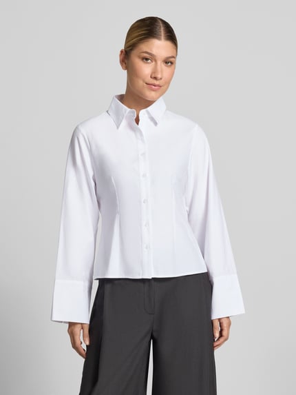 Frauenmodel trägt Oversized Fit Hemdbluse aus Baumwoll-Mix mit Ziernähten von Neo Noir in Weiß, klare Knopfleiste, schwarze Hose, Nahaufnahme Oberkörper. Damen Hemdbluse mit Hemdblusenkragen, langärmligem Design, 1-Knopf-Manschetten, Rückenlänge 55 cm, Ärmellänge 61 cm.