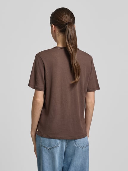 Modelka kobieca ma na sobie Regular Fit T-Shirt aus Leinen-Mix mit V-Ausschnitt od Scotch & Soda, brązowy, ażurowy wzór, krój regular fit, długość tyłu w rozmiarze S: 62 cm, widok całej sylwetki z tyłu.