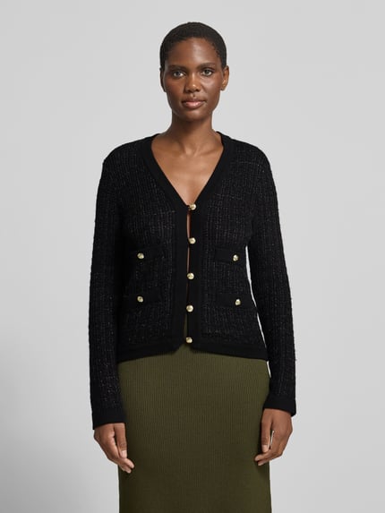 Frauenmodel trägt Cardigan mit goldfarbenen Zierknöpfen von Anine Bing in schwarzer Strickoptik mit Strukturmuster, Ganzkörperansicht von vorne.