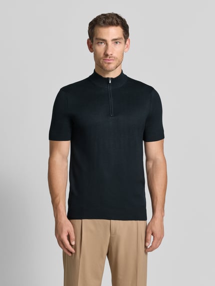 Männermodel trägt Strickshirt aus Viskose-Mix mit Stehkragen Modell 'Vadin' von JOOP!, Schwarz, Reißverschluss, Ganzkörperansicht von vorne. Körpernaher Schnitt mit kurzem Arm, Rückenlänge 68 cm, Ärmellänge 24 cm.