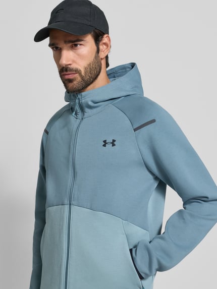 Männermodel trägt Kurtka treningowa z mieszanki materiałów z bawełną, krój regular fit, kaptur, zamek błyskawiczny dwustronny, model 'Unstoppable' od Under Armour, długość tyłu 71 cm, długość rękawów 60 cm, widok z przodu, zbliżenie na górną część.