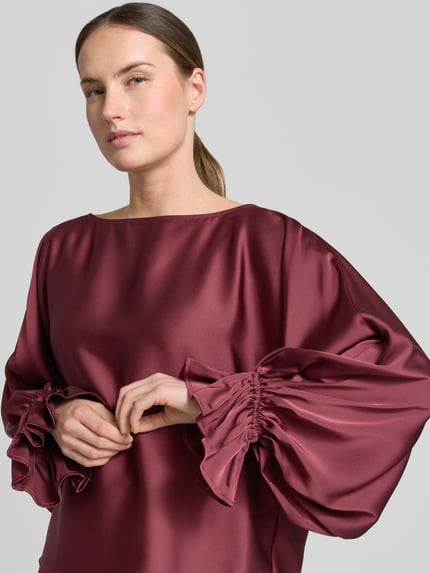 Modelka kobieca ma na sobie Blusenshirt aus Satin mit Rundhalsausschnitt od V by Vera Mont, satyna, krój regular fit, rękawy typu trąbka, kolor bordowy, tekstura gładka, zbliżenie na górną część ciała