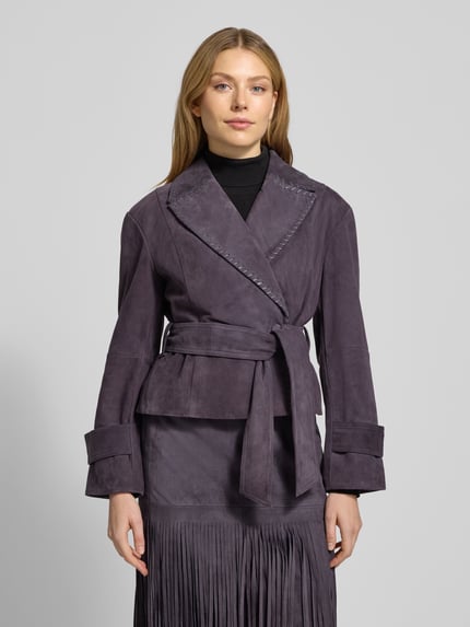 Frauenmodel trägt Lederjacke mit Bindegürtel von Marc Cain in Dunkellila, taillierter Schnitt, Reverskragen, Ganzkörperansicht von vorne.