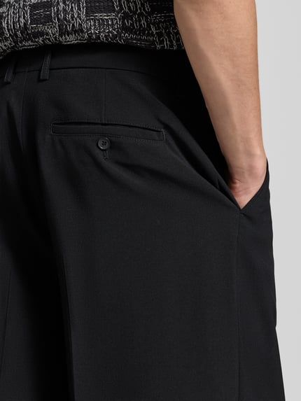Männermodel trägt Relaxed Fit Stoffhose aus Woll-Mix von Filippa K, schwarz, Bundfalten, Gesäßtasche, Nahaufnahme Rückansicht.