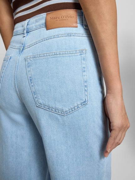 Frauenmodel trägt Wide Leg Hose aus Baumwoll-Mix Modell 'TOLVA LONG' von Marc O'Polo in hellem Denim, 5-Pocket-Design, Label Patch, Detailaufnahme Rückansicht.