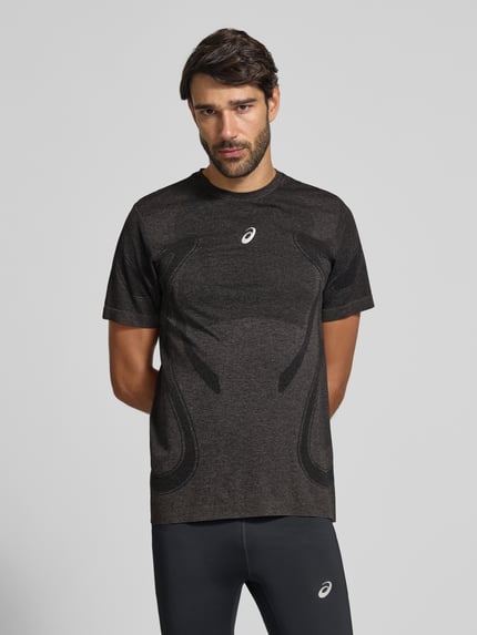 Męskimodel nosi męski t-shirt Slim Fit RUNNING T-Shirt Model 'ROAD' od ASICS, krój slim fit, okrągły dekolt, nadruk z logo w kolorze metallic, długość tyłu w rozmiarze M: 72 cm, ciemnoszary melanż, gładka tekstura, całkowity widok z przodu.