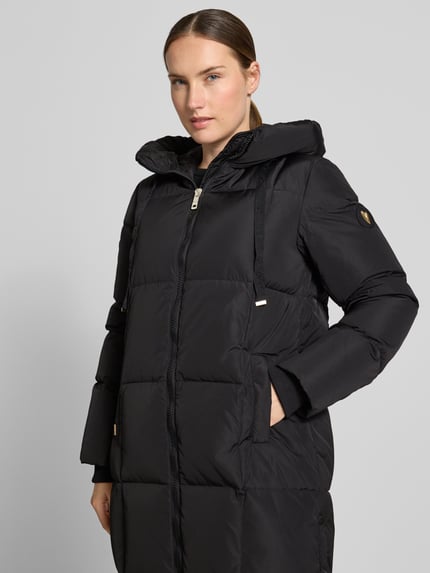 Kobiece modelka nosi czarny płaszcz z efektem pikowania, kaptur z tunelem, wpuszczane kieszenie, model 'Nova' od MOS MOSH, krój regular fit, długość tyłu w rozmiarze S: 102 cm, szerokość ramion w rozmiarze S: 42 cm, szerokość w rozmiarze S: 46 cm, długość rękawów w rozmiarze S: 64 cm, zamek błyskawiczny dwustronny, wpuszczane kieszenie, zdjęcie: zbliżenie na górną część ciała z przodu.