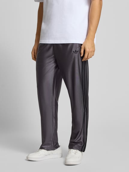 Männermodel draagt Jogpants mit Label-Stitching Modell 'FIREBIRD' van adidas Originals, grijs met zwarte details, Ganzkörperansicht van voren.