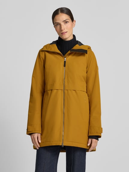 Frauenmodel trägt Regular Fit Parka mit Kapuze von Didriksons in Senfgelb mit Eingrifftaschen, Zweiwege-Reißverschluss, Ganzkörperansicht von vorne. Rückenlänge, Schulterbreite, Brustweite und Ärmellänge jeweils passend zur Größe 36.