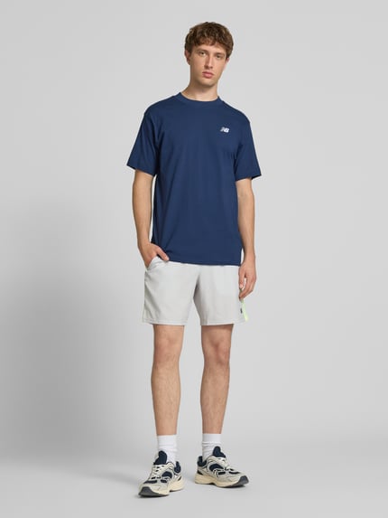 Männermodel trägt T-Shirt mit Logo und Rundhalsausschnitt von New Balance in Dunkelblau, Reine Baumwolle, Regular-Fit, Ganzkörperansicht von vorne. Rückenlänge bei Größe M: 74 cm.