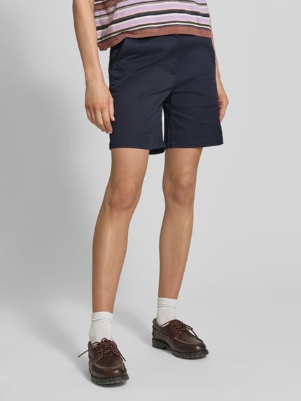 Kobiece model nosi Bermudas mit Gesäßleistentaschen od Gant z bawełnianej mieszanki z elastanem, krój straight fit, granatowy kolor, szerokość w rozmiarze 36: 38 cm, długość wewnętrzna nogawki: 18 cm, widok całej sylwetki z przodu.