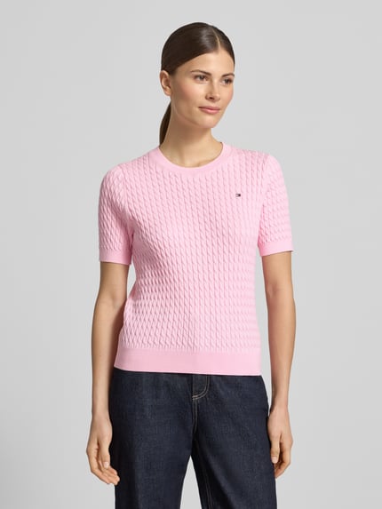 Frauenmodel trägt Slim Fit T-Shirt aus reiner Baumwolle von Tommy Hilfiger in Optik: Unifarben mit Zopfmuster, Logo-Detail, Strick, Ganzkörperansicht von vorne.