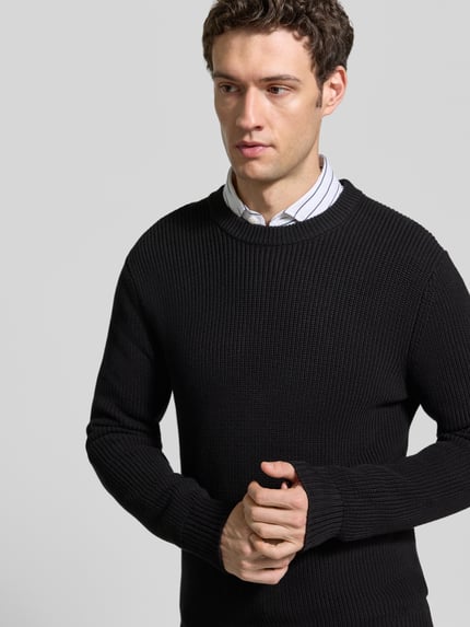 Männermodel trägt Regular Fit Strickpullover aus reiner Baumwolle von MCNEAL, schwarze Farbe, strukturierte Oberfläche, Nahaufnahme Oberkörper. Rückenlänge 73 cm, Ärmellänge 53 cm, Rundhalsausschnitt, elastische Abschlüsse.