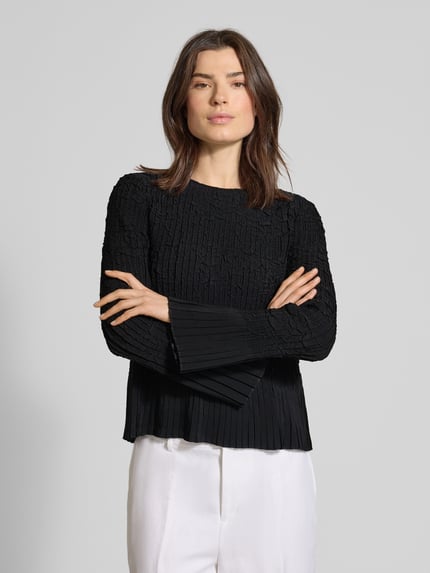 Vrouwenmodel draagt Regular Fit Langarmbluse in crinkle-look model 'BOPPAR' van BOSS, zwart, ronde hals met V-hals, lange geplooide mouwen, unikleuren, materiaal in crinkle-structuur, close-up bovenlichaam.